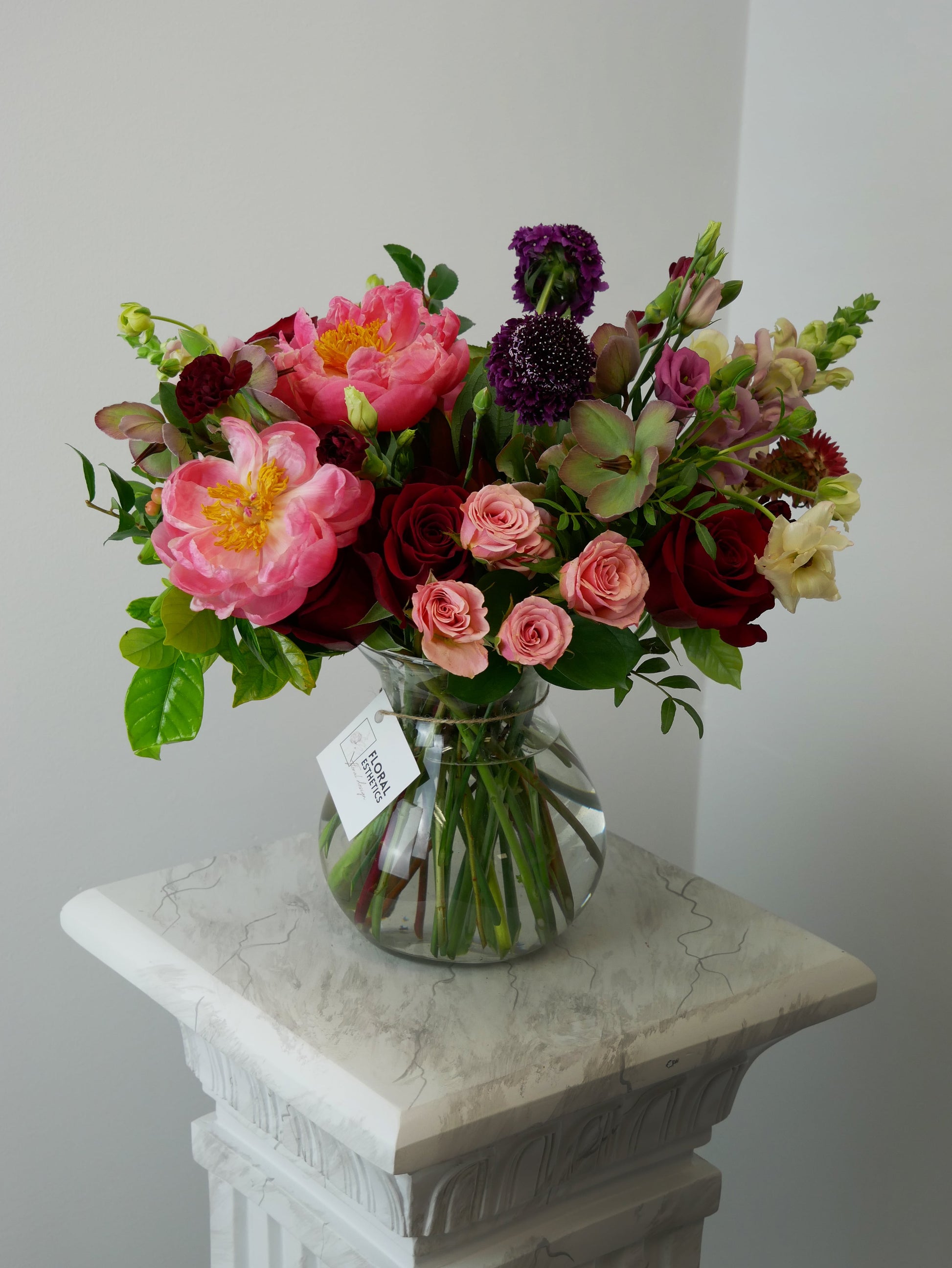 Premium burgundy red and pink flower arrangement in vase featuring peonies, roses, hellebore and rich foliage by Floral Esthetics