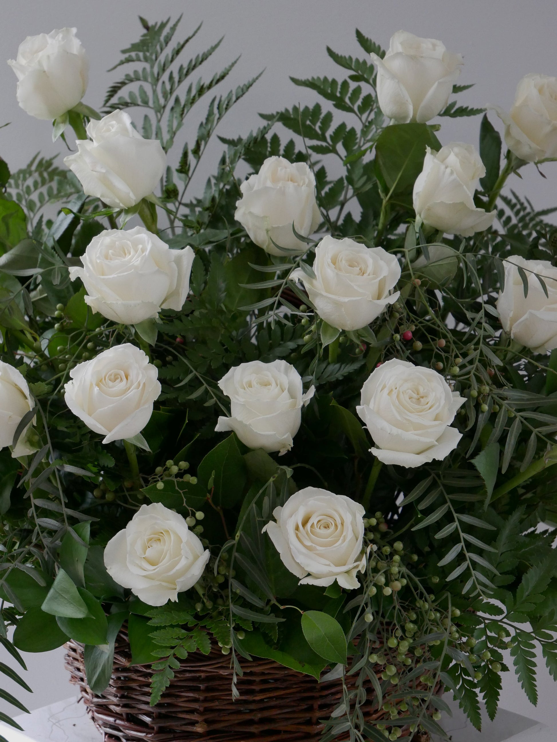Close up on elegant flower basket featuring 2 dozen white roses and premium foliage by Floral Esthetics