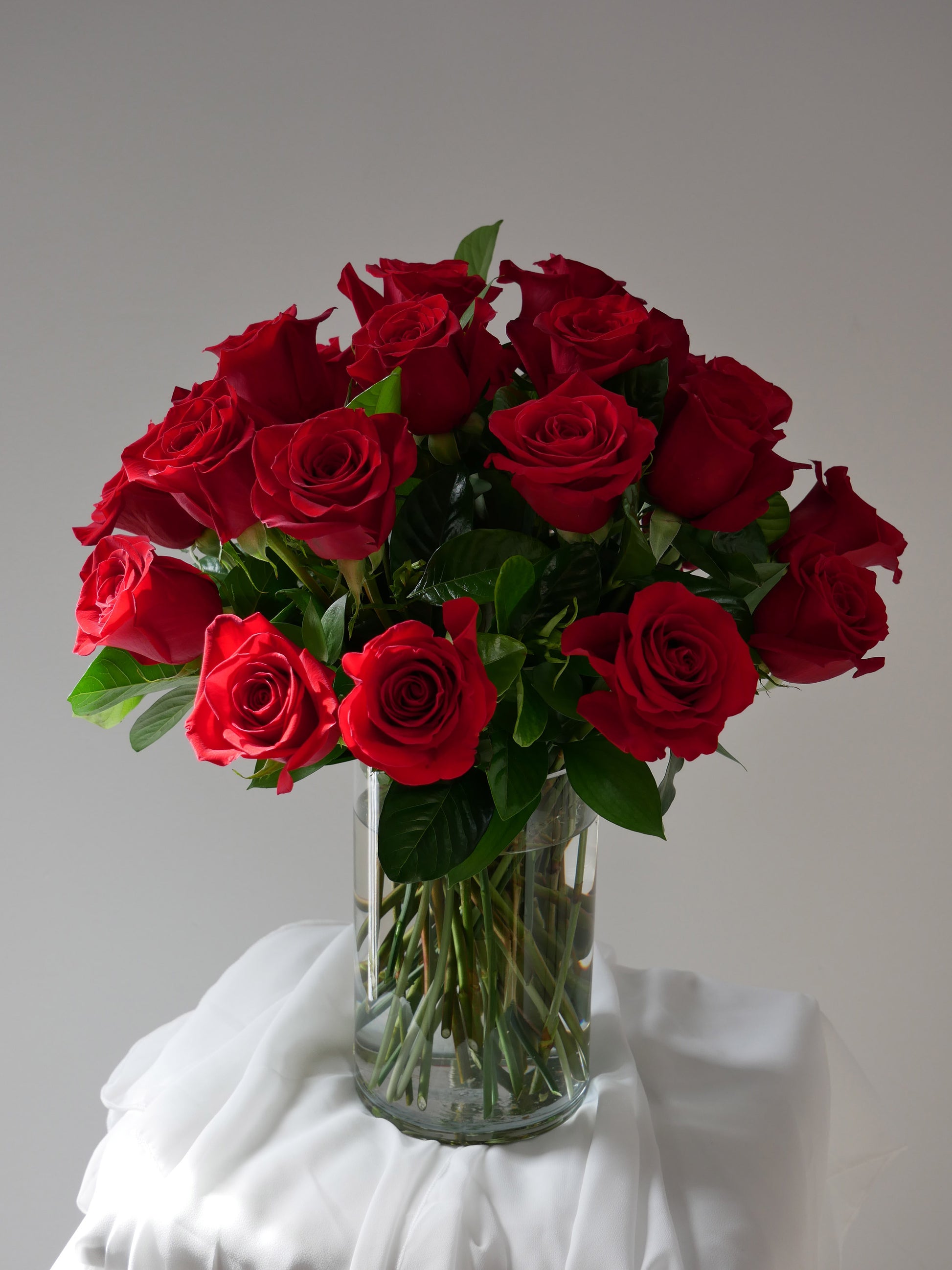 Two dozen red roses with premium greenery in clear cylinder by Floral Esthetics 