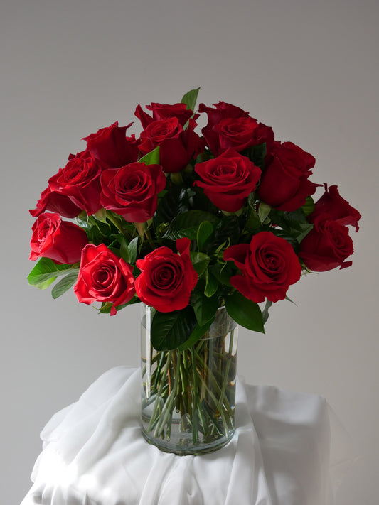 Two dozen red roses with premium greenery in clear cylinder by Floral Esthetics 