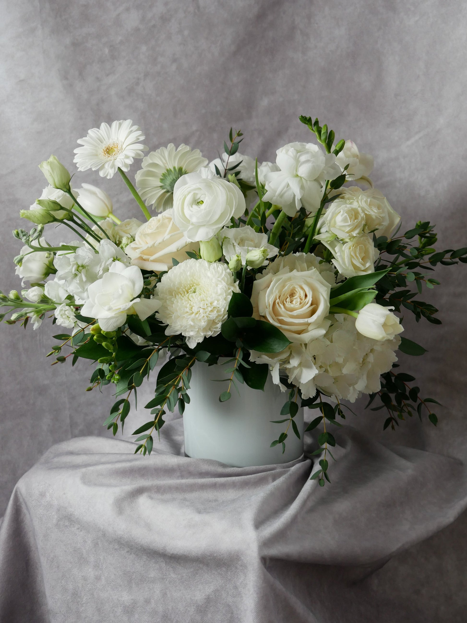 white flower arrangement in what low cylinder featuring hydrangea, ranunculus, gerberas, roses and more 