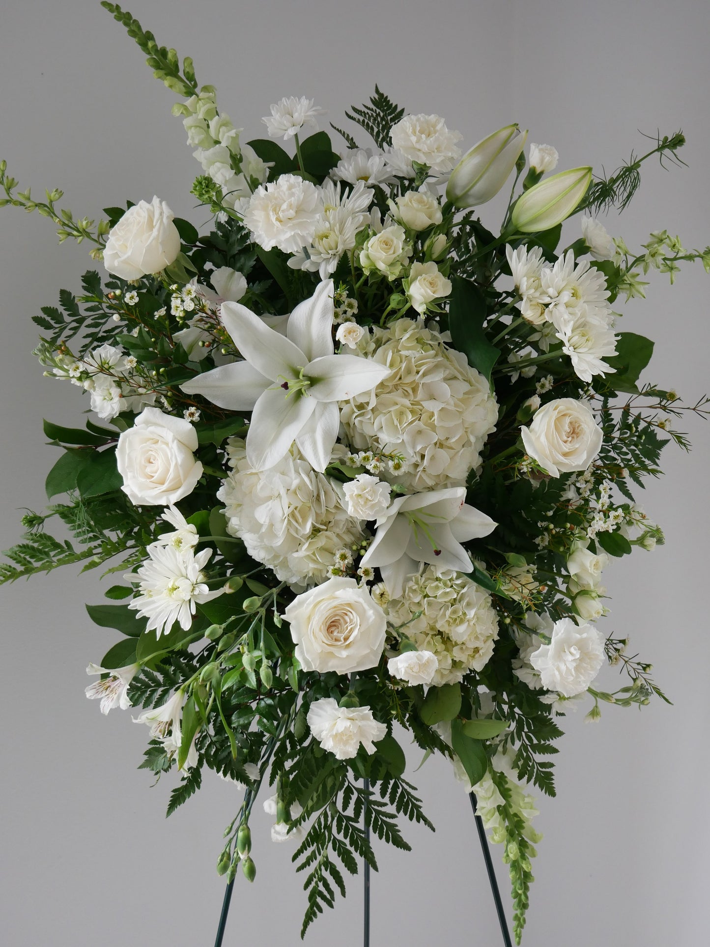 White funeral spray featuring lily, roses, spray roses, chrysanthemum, carnations, snap dragon and greens