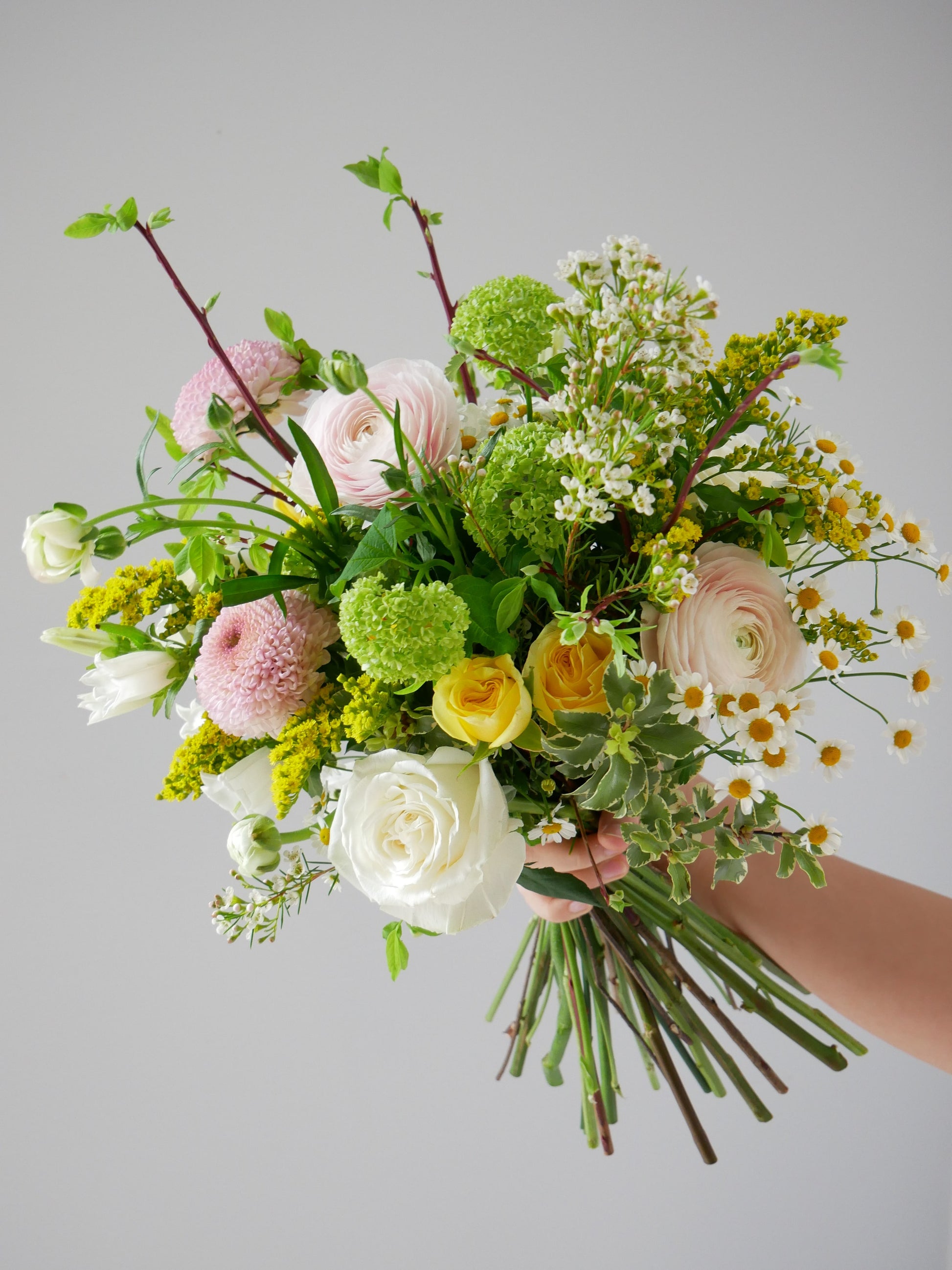 Bouquet in garden style featuring light pink ranunculus, chrysanthemum, white roses, yellow spray roses, viburnum and more