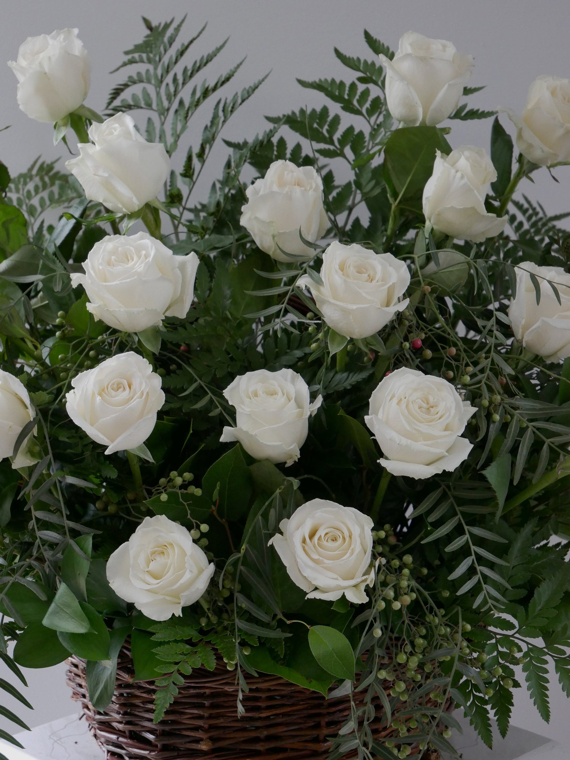 Close up on elegant flower basket featuring 2 dozen white roses and premium foliage