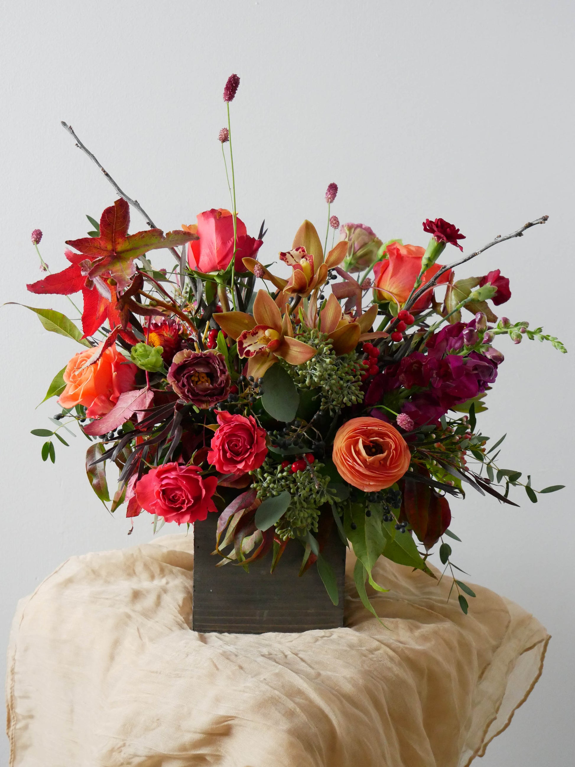 Colorful floral arrangement in a wooden box on a light fabric surface with a neutral background