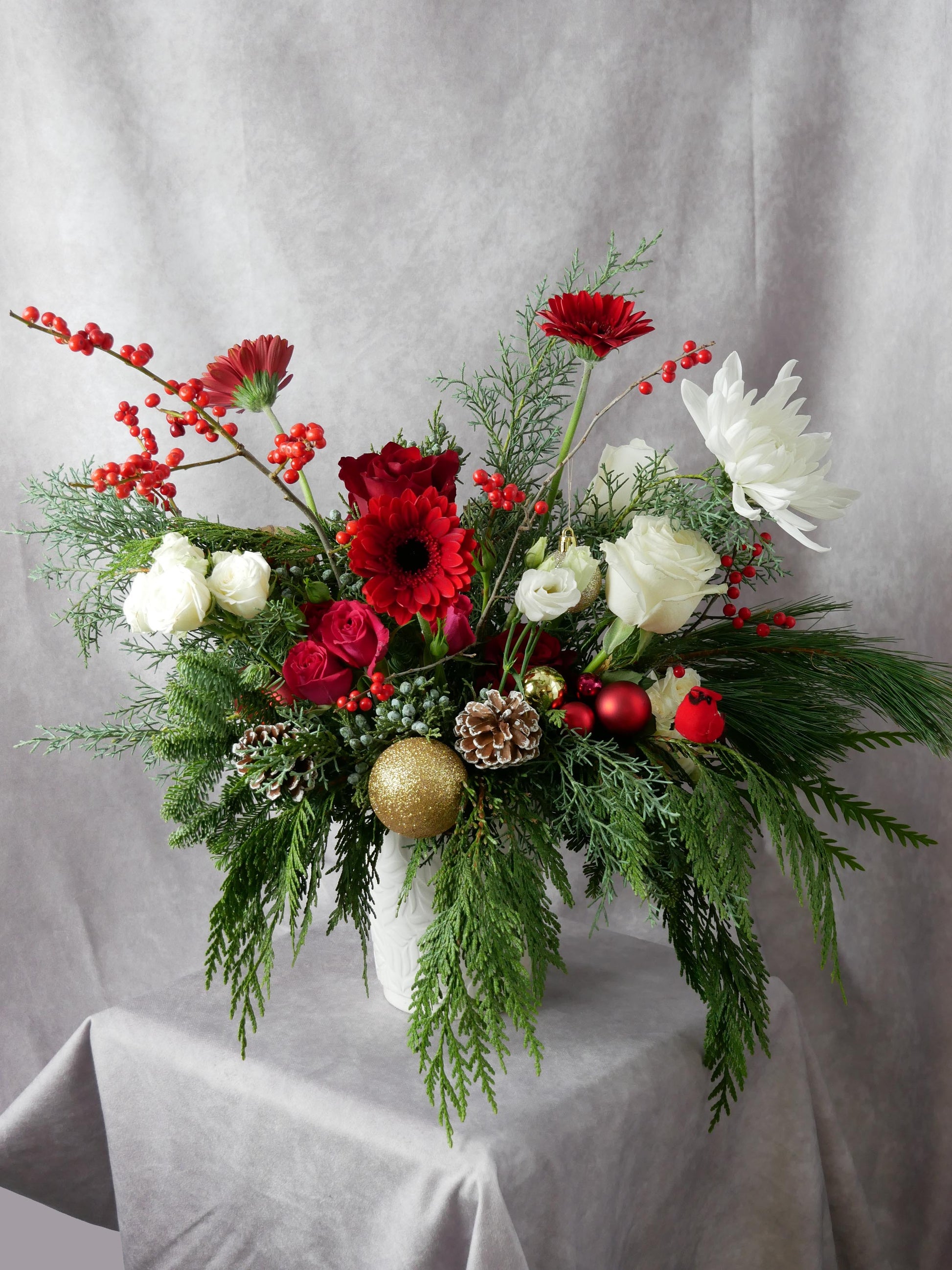 Christmas arrangemennt featuring Ilex berries, pine cones, noble twigs, eucalyptus, white roses, spray roses, lisianthus, red mini gerberas, aster and other flowers by Floral Esthetics