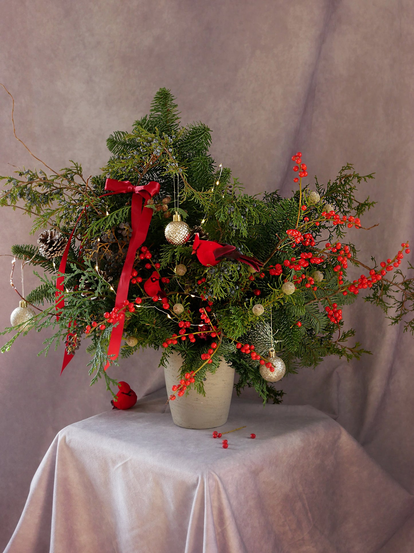 Christmas Magic arrangement featuring noble fir, Incense cedar, pine tree, Ilex berries, pine cones and matching color toys. By Floral Esthetics