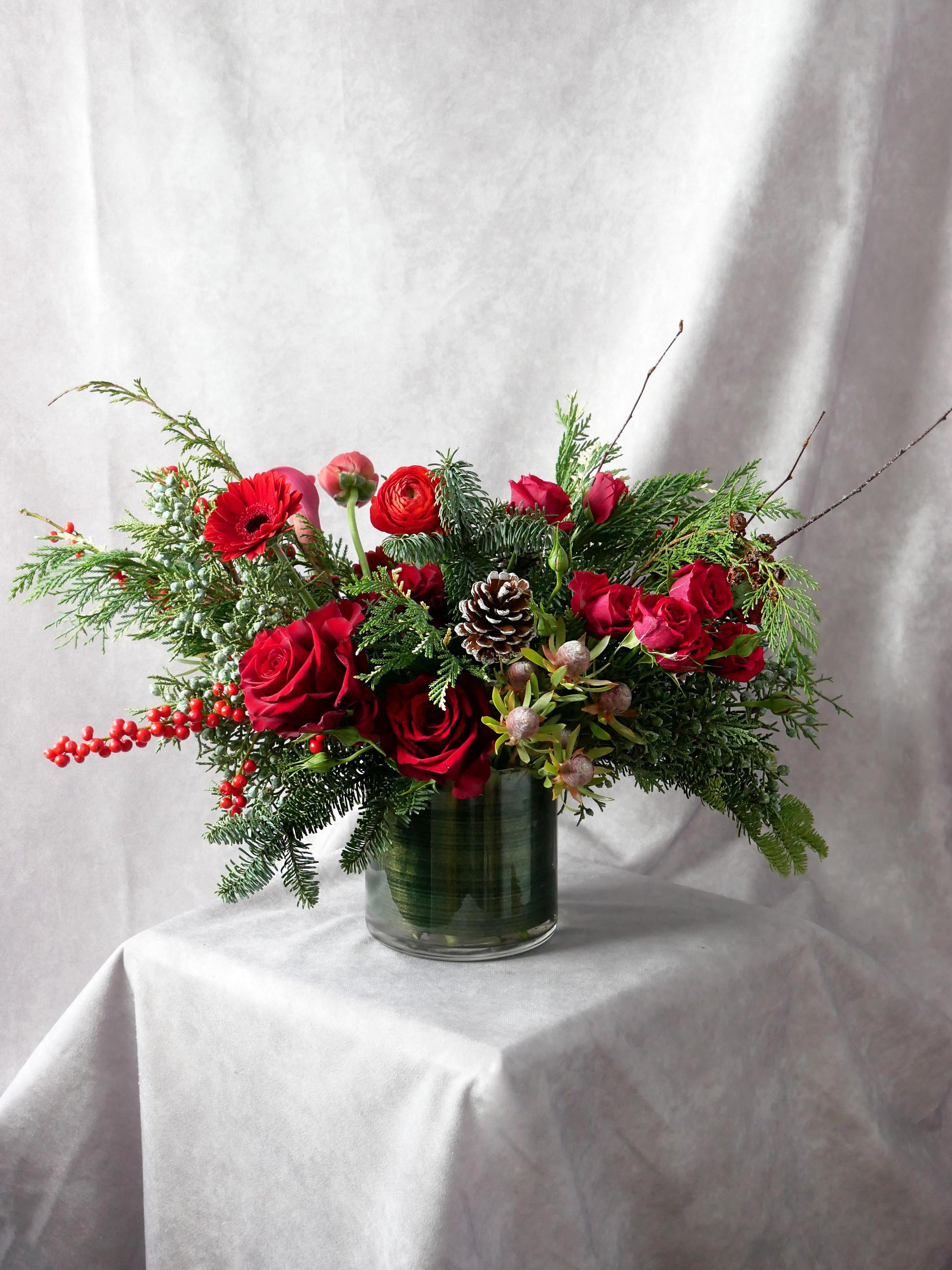 Christmas Spirit arrangement #2 featuring seasonal greens and red blooms such as roses, gerberas, lilies, ranunkulus, ilex berries and more. By Floral Esthetics