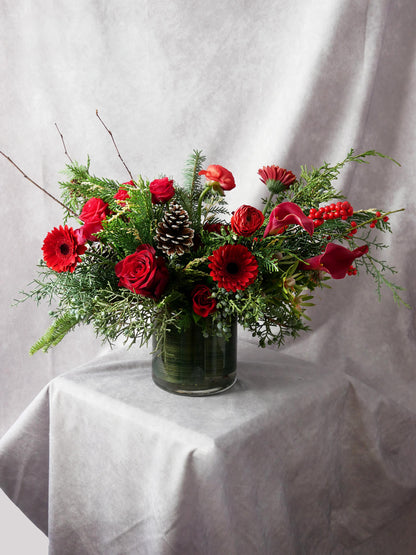 Christmas Spirit arrangement featuring seasonal greens and red blooms such as roses, gerberas, lilies, ranunkulus, ilex berries and more. By Floral Esthetics