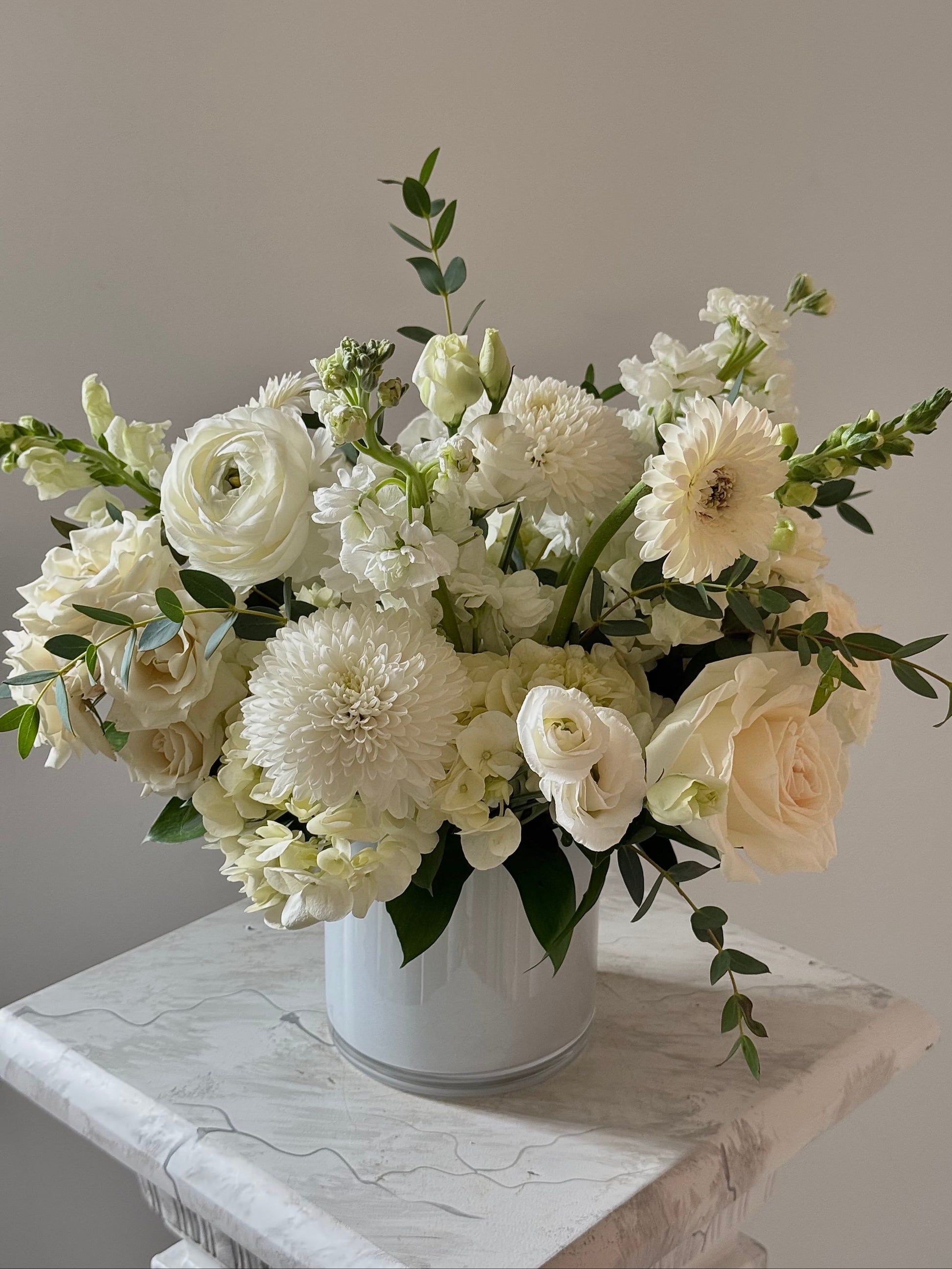 Bouquet of white flowers in a white vase on a marble surface with a neutral background