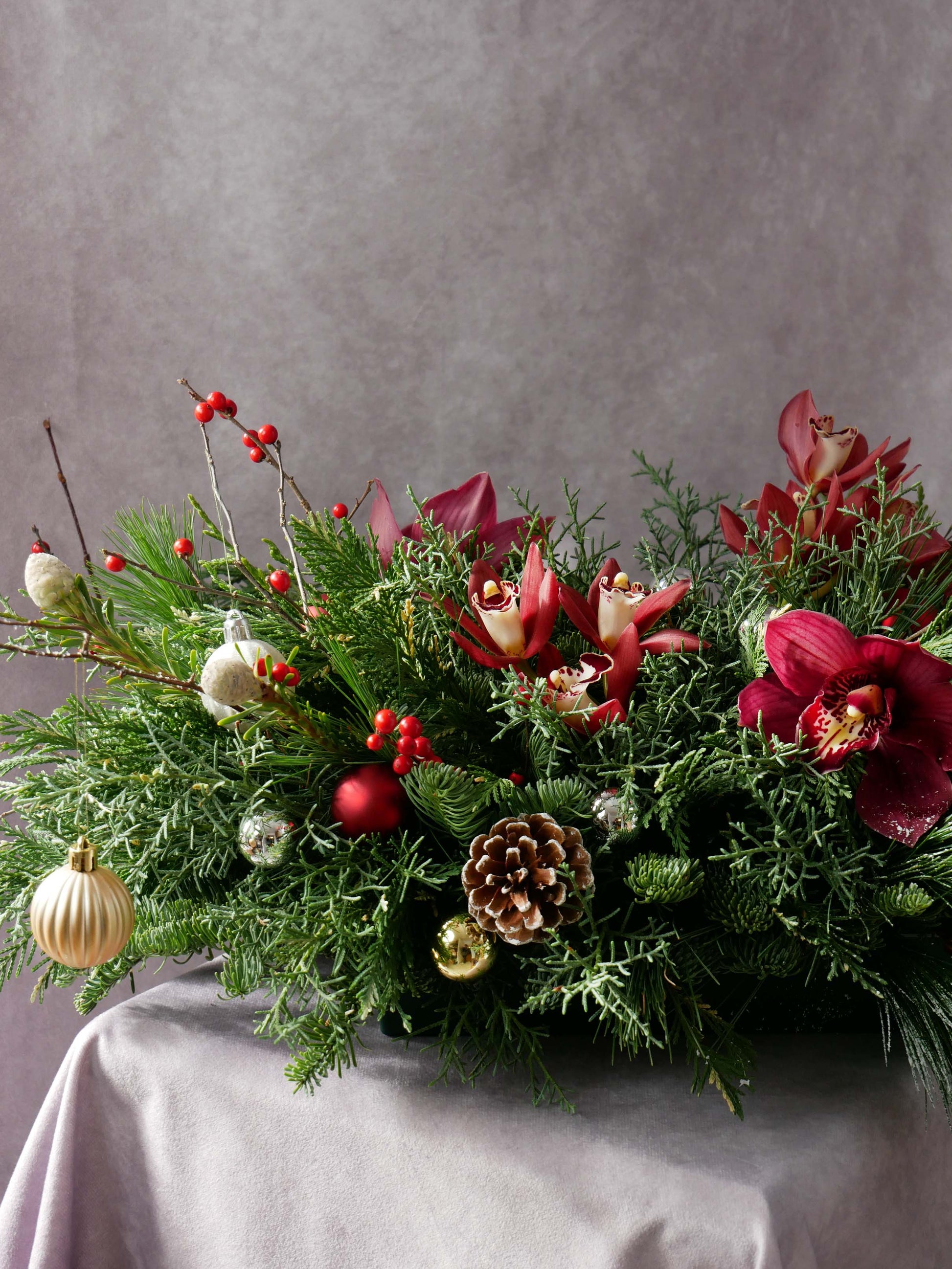 Close-up on Holiday Centerpiece with Orchids and Seasonal greens and berries and also featuring Christmas ornaments and toys. By Floral Esthetics