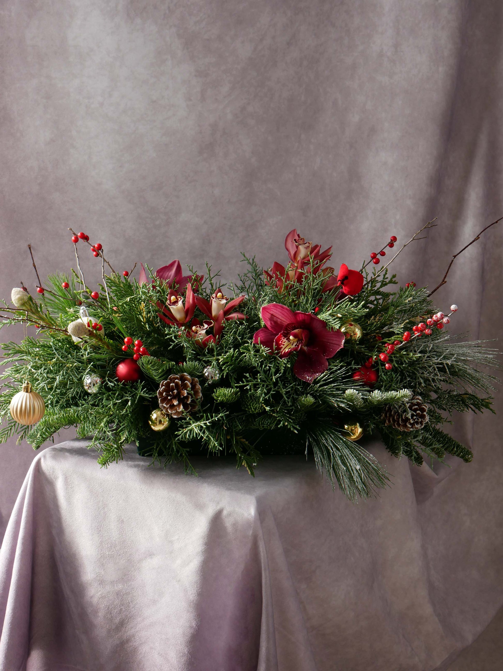 Holiday Centerpiece with Orchids and Seasonal greens and berries and also featuring Christmas ornaments and toys. By Floral Esthetics