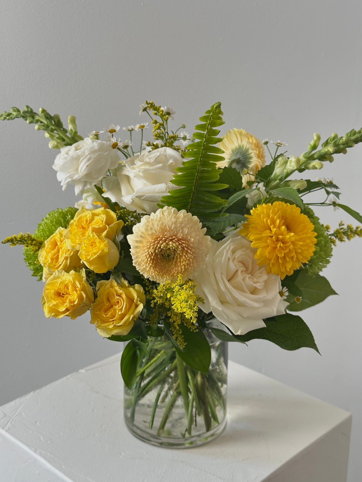 Bouquet of yellow and white flowers in a clear vase on a light surface with a neutral background