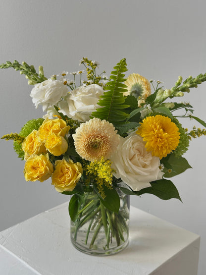Bouquet of yellow and white flowers in a clear vase on a light surface with a neutral background