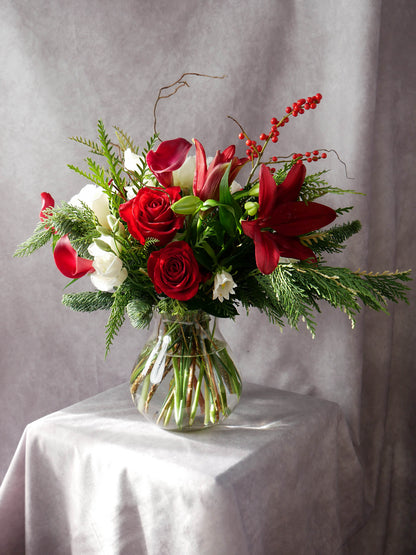 Merry Christmas Arrangement  featuring seasonal greens and blooms such as noble fir, Incense cedar, pine tree, Ilex berries, pine cones, roses, lilies, chrysanthemums and more. By Floral Esthetics   