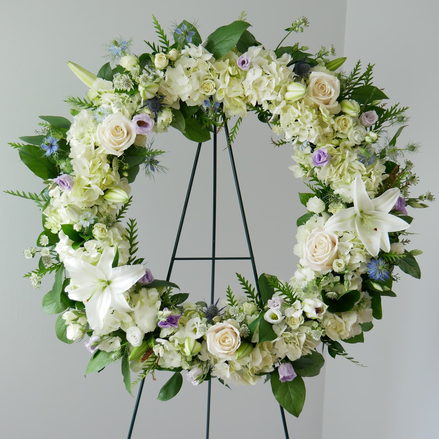 Funeral white wreath with pop of purple. Featuring hydrangea, lilies, roses and other by Floral Esthetics