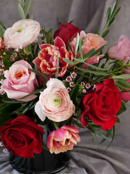 Close-up on Passion in Bloom flower arrangement in low black glass cylinder features roses, ranunculus, tulips and lash greens