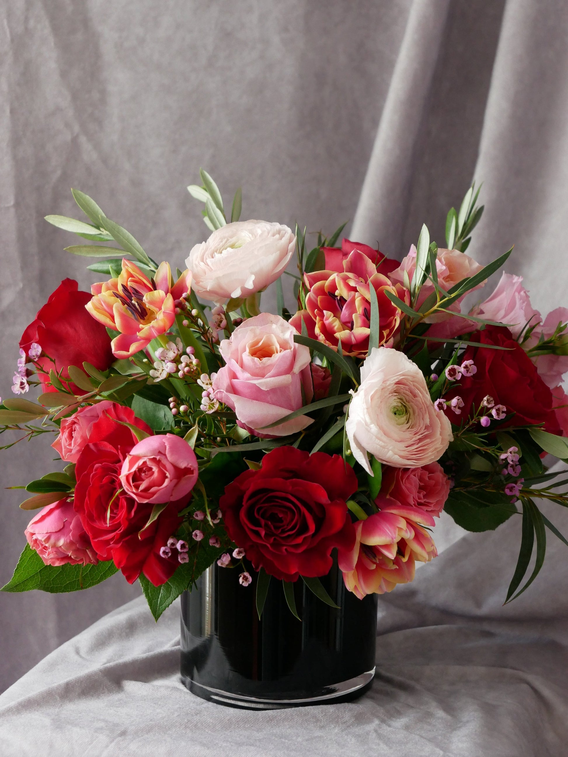 Passion in Bloom flower arrangement in low black glass cylinder features roses, ranunculus, tulips and lash greens by Floral Esthetics