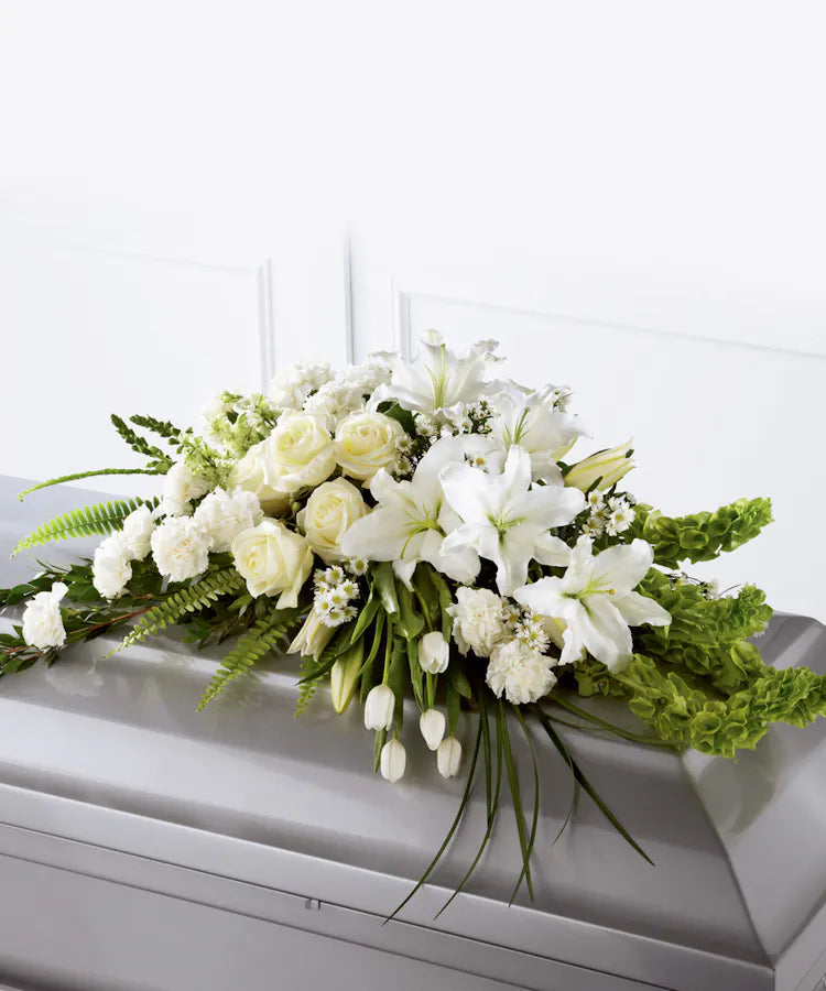 White casket spray featuring white lilies, roses, tulips, carnations and different greenery  