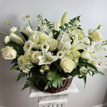 Large white sympathy floral basket featuring lilies, roses, hydrangeas, gerberas, greens and more