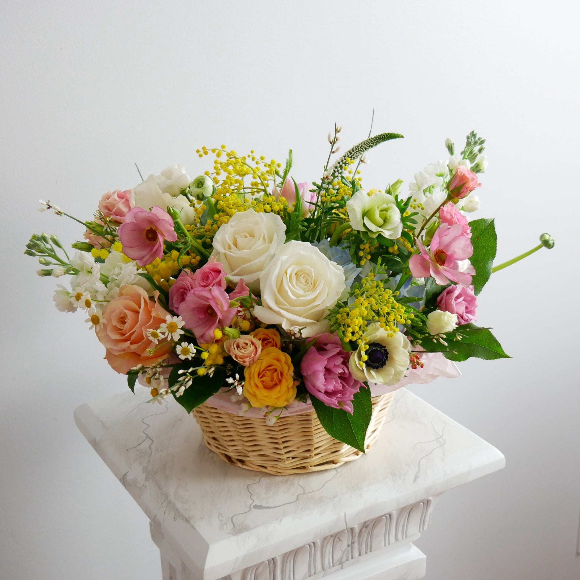 Spring medium size flower basket featuring white roses, mimosa, anemone, pink ranunculus, tulips and more