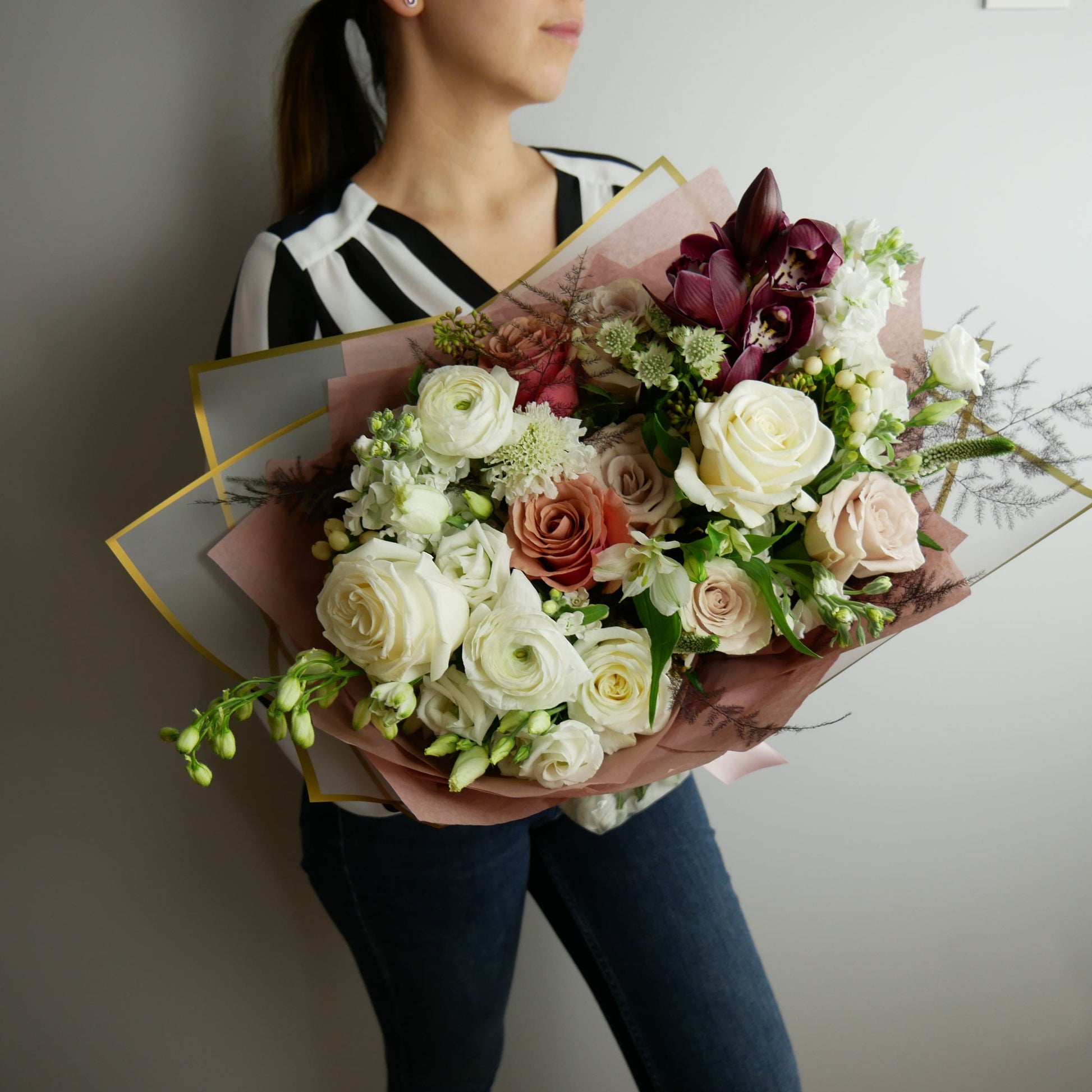 White and coffee color wrapped bouquet featuring orchids, ranunculus, roses, spray roses, lizianthus,  and more