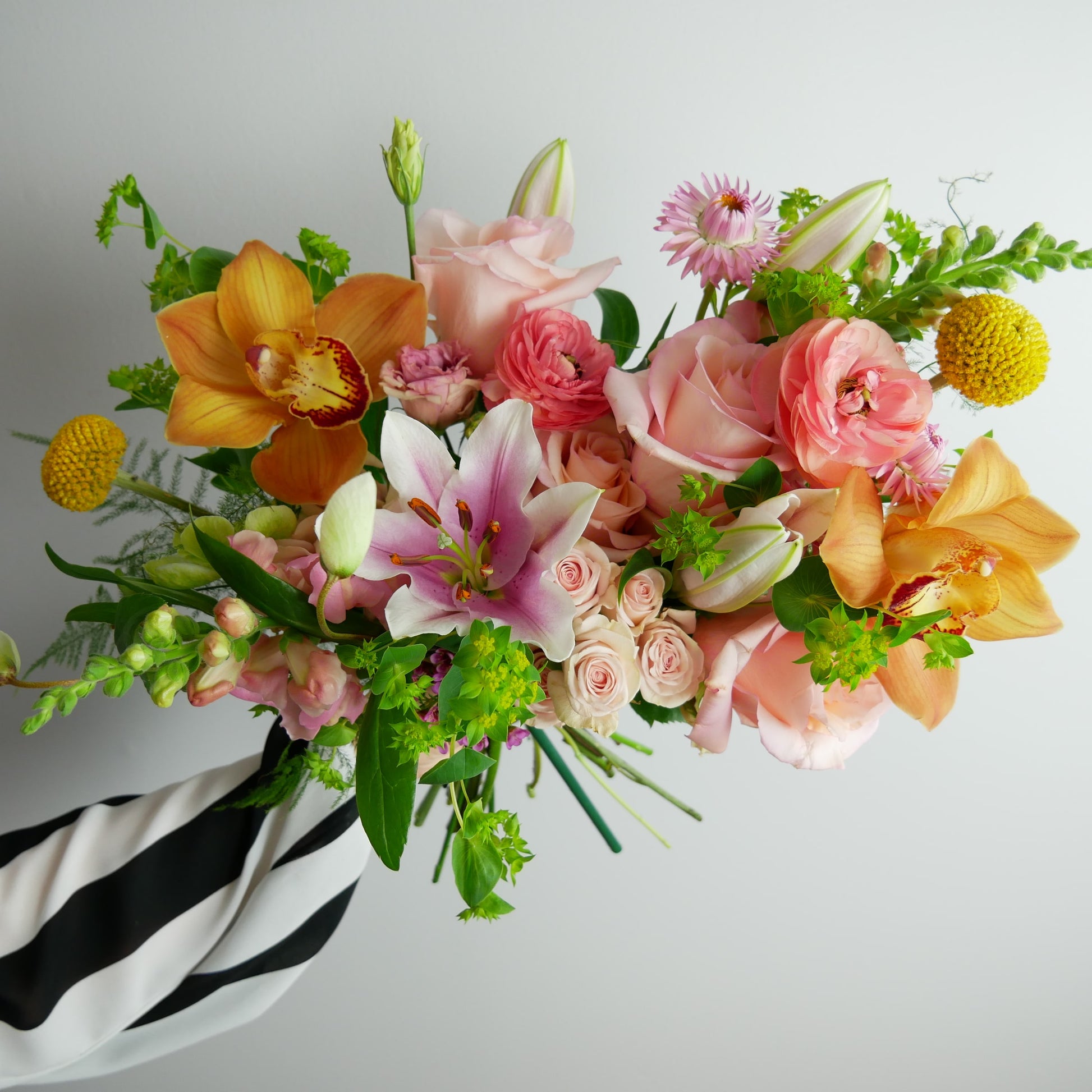 Different angle of Bright tropical bouquet featuring orchids, lilies, ranunculus, craspedia, roses, snap dragon and much more