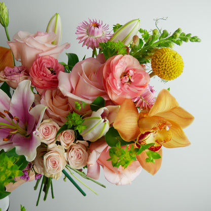 Close-up on Bright tropical bouquet featuring orchids, lilies, ranunculus, craspedia, roses, snap dragon and much more
