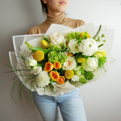Premium size wrapped bouquet inn white, green and yellow colors. Featuring ranunculus, roses, hydrangeas, greens and more