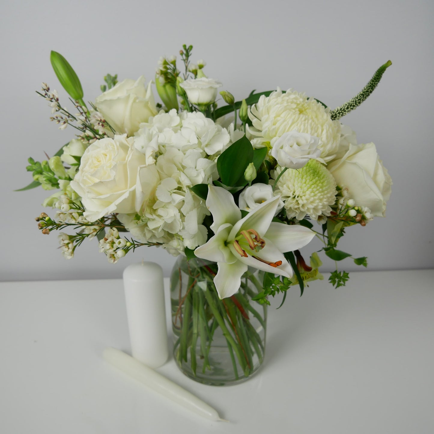 White flower arrangement in clear vase featuring lilies roses, chrysanthemum and more