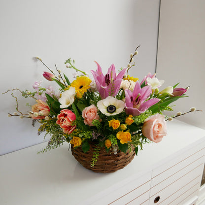 Spring medium size flower basket featuring pink lilies, white anemone, peach roses, orange tulips, yellow accents, pussy willow and more