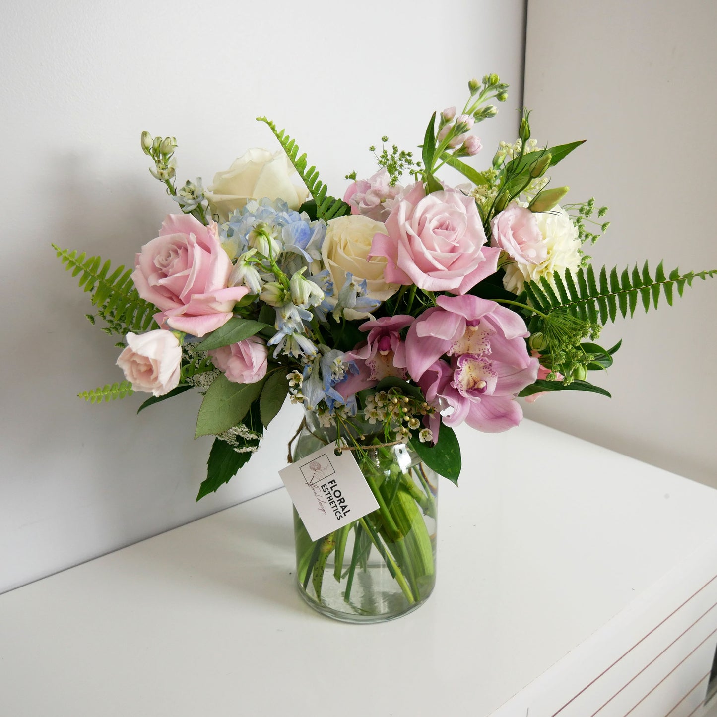 Pastel color premium size flower arrangement in clear vase featuring pink orchids and roses, white roses, delphinium, lizianthus and more