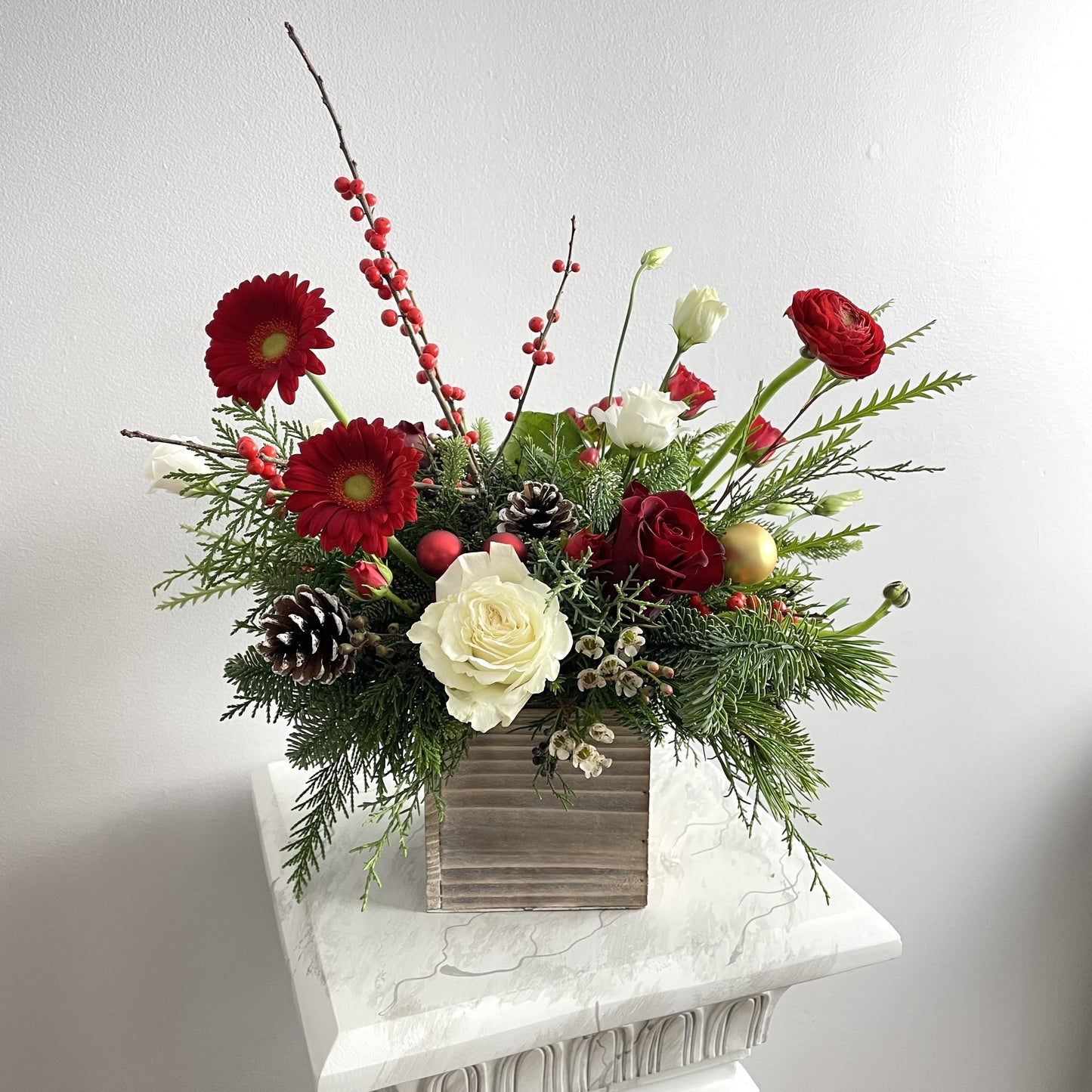 Christmas arrangemennt in wooden box featuring Ilex berries, pine cones, noble twigs, red roses roses, spray roses, lisianthus, red mini gerberas, aster and other flowers by Floral Esthetics