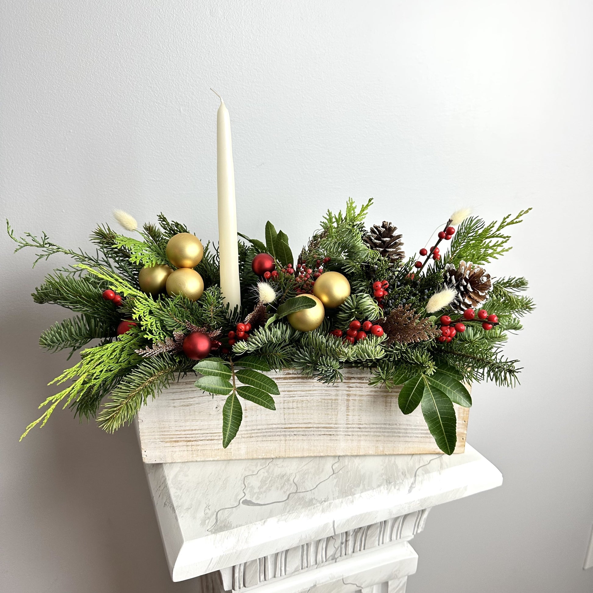 Long lasting Christmas Arrangement in wooden box with candles featuring noble fir, Incense cedar, pine tree and more. We also added Ilex berries, pine cones and matching color toys. By Floral Esthetics