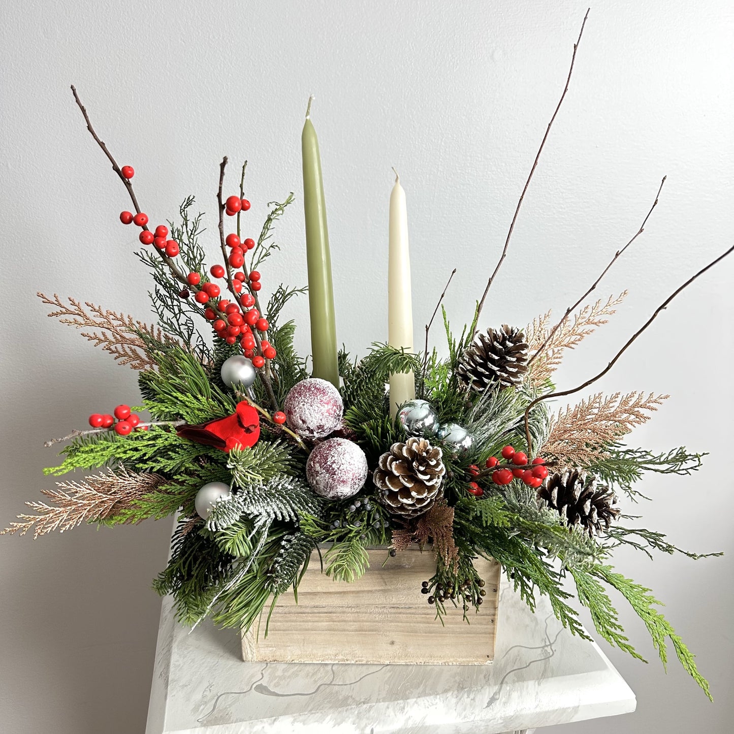 Long lasting Christmas Arrangement in wooden box with candles featuring noble fir, Incense cedar, pine tree, Ilex berries, pine cones and matching color toys. By Floral Esthetics