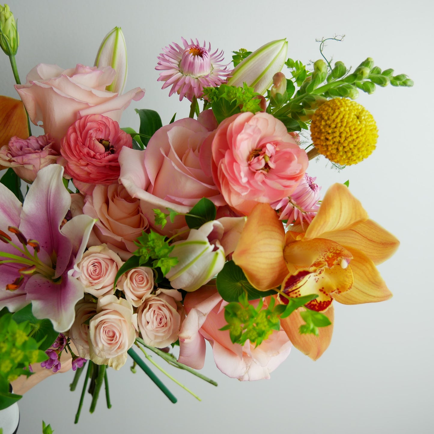 Close-up on Bright tropical bouquet featuring orchids, lilies, ranunculus, craspedia, roses, snap dragon and much more by Floral Esthetics