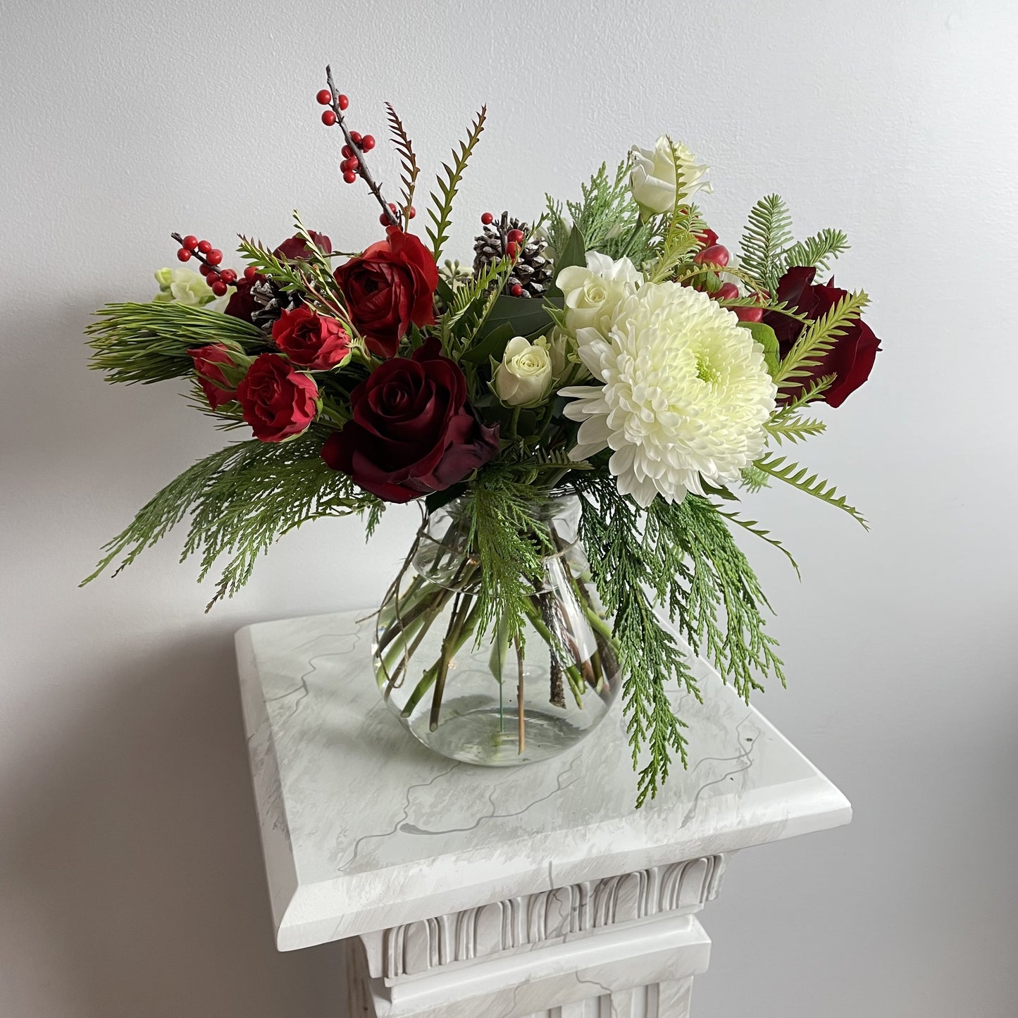 Merry Christmas Arrangement  featuring seasonal greens and blooms such as noble fir, Incense cedar, pine tree, Ilex berries, pine cones, roses, ranunculus, chrysanthemums and more. By Floral Esthetics   