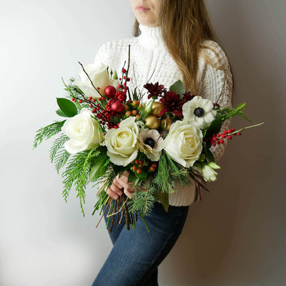 Merry Christmas Bouquet featuring seasonal greens and blooms such as noble fir, Incense cedar, pine tree, Ilex berries, pine cones, roses, anemones, chrysanthemums and more. By Floral Esthetics   