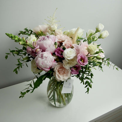 Tender pink and white standard size flower arrangement in clear vase featuring peonies, ranunculus, roses, greens and more by Floral Esthetics