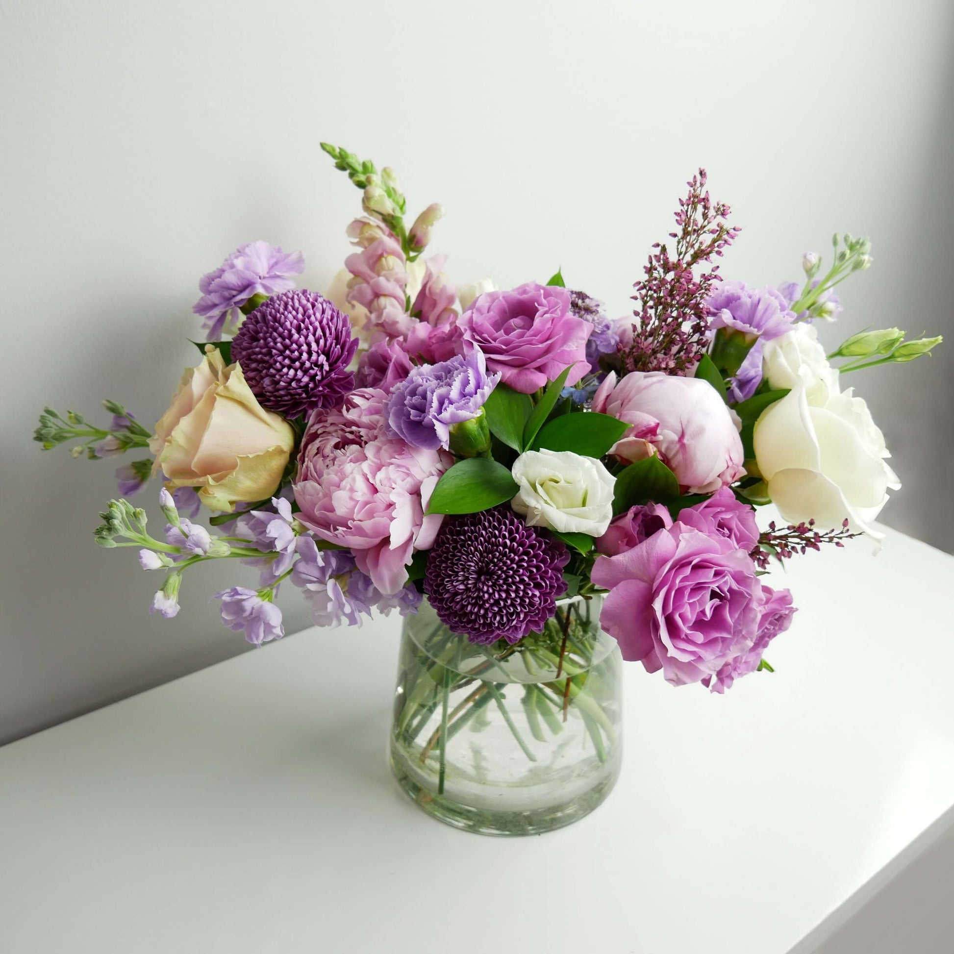 Premium white and purple flower arrangement in low vase featuring peonies, chrysanthemum and roses by Floral Esthetics in Marstons Mills, MA