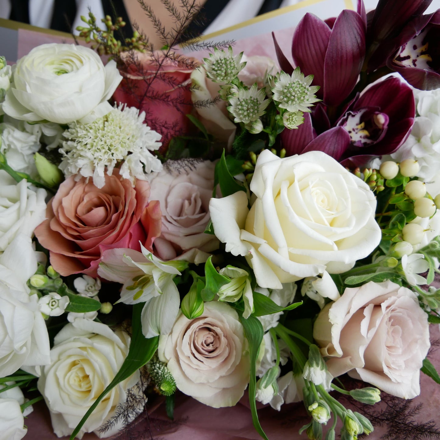 Close-up on White and coffee color wrapped bouquet featuring orchids, ranunculus, roses, spray roses, lizianthus, and more by Floral Esthetics