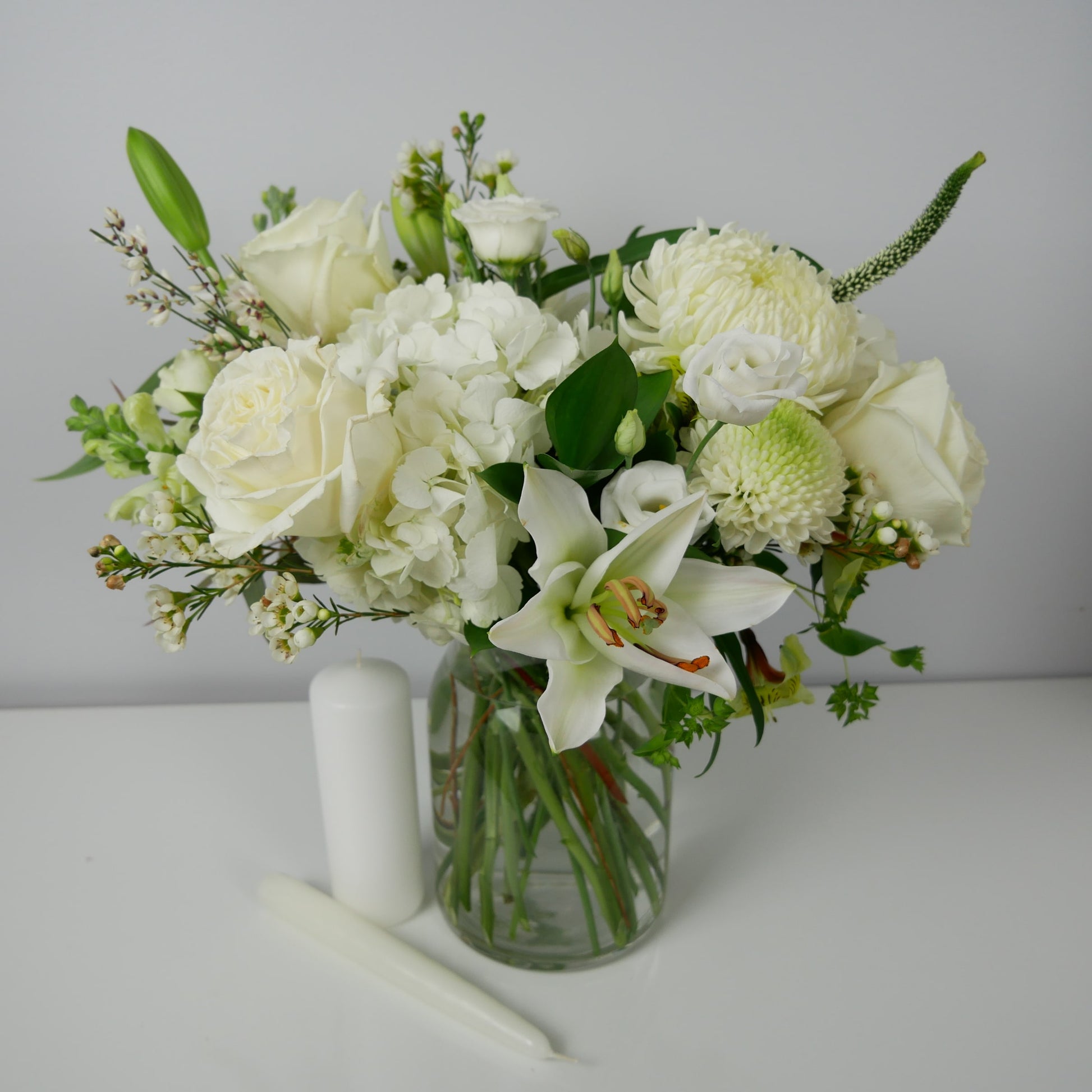 White flower arrangement in clear vase featuring lilies roses, chrysanthemum and more by Floral Esthetics