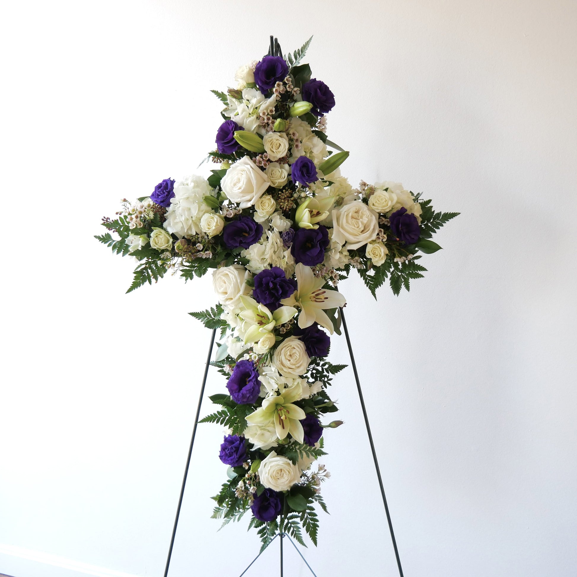 Standing flower cross featuring white lilies, roses and hydrangeas with pops of purple lizianthus by Floral Esthetics